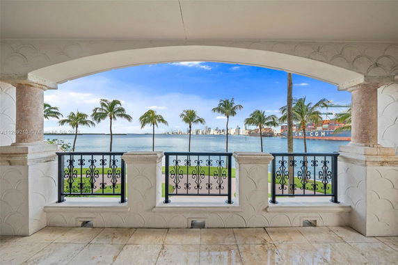 Balcony view overlooking a body of water with palm trees and a distant city skyline.