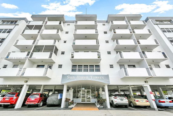 Front view of a multi-story building with balconies and a parking area beneath.