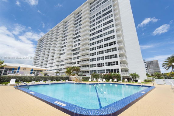 View of a large residential building with a swimming pool in front.