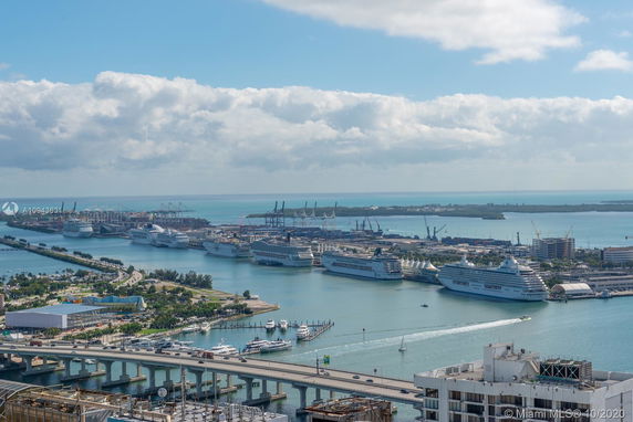 Panoramic view overlooking a harbor with multiple cruise ships docked, surrounded by water and a bridge in the foreground.
