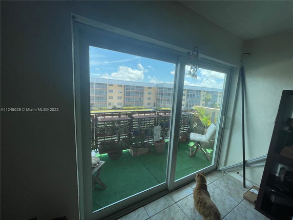 View of residential buildings seen through a glass sliding door with a balcony in the foreground.