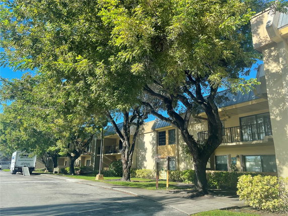 Front view of a two-story building with a balcony and large trees nearby.