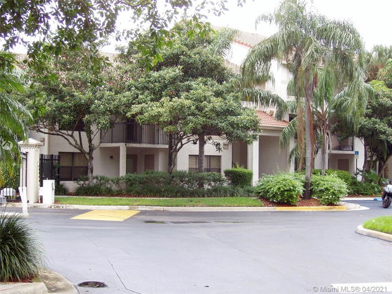 Front view of a multi-story building with balconies and surrounded by trees.