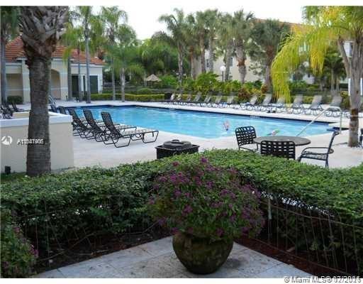 Outdoor swimming pool area with lounge chairs and tables surrounded by palm trees.