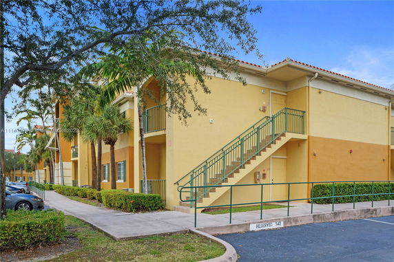 Front view of a two-story apartment building with exterior stairs and yellow and orange walls.