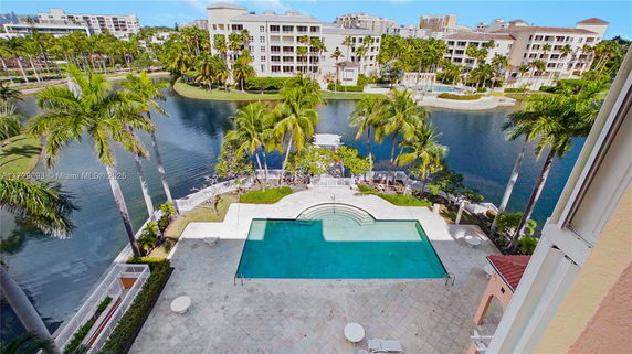 View of a swimming pool with surrounding palm trees and a water body beyond.