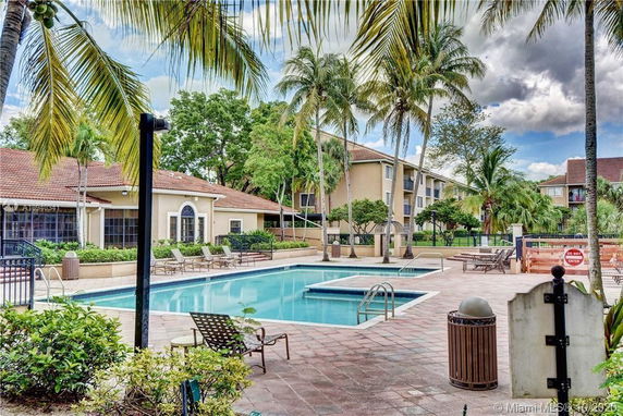 Outdoor view of a swimming pool area near residential buildings with palm trees and lounge chairs.