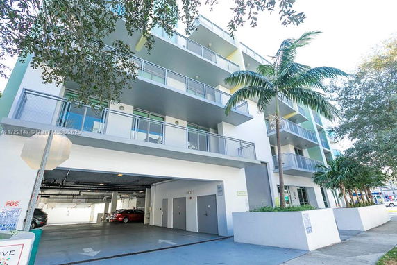 Front view of a multi-story building with balconies and parking area below.