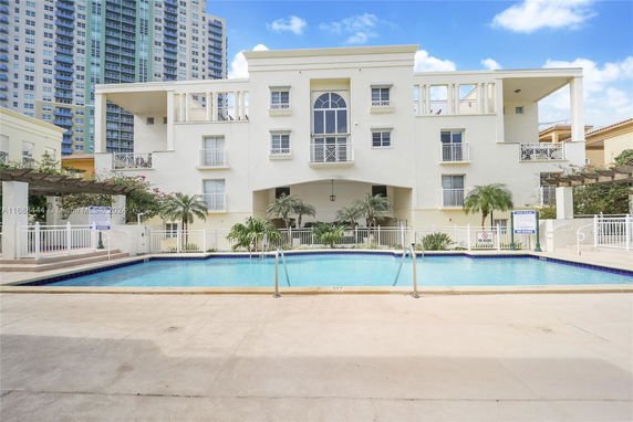 Facade of a white multi-story building with a rectangular swimming pool in the foreground.