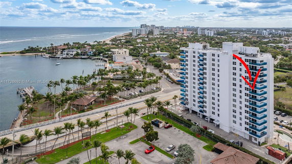 Aerial view of a coastal building with ocean and nearby residential area.