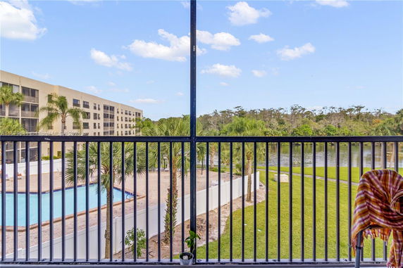 View from a balcony overlooking a swimming pool, building, and greenery.