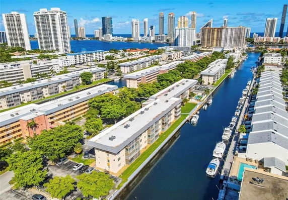 Aerial view of residential buildings along a canal with boats, surrounded by high-rise structures in the distance.