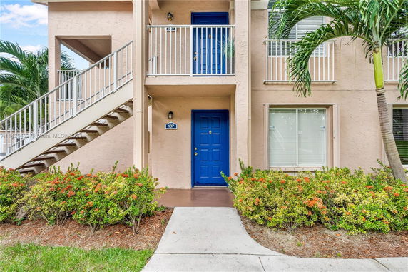 Front view of a beige apartment building with blue doors and a staircase leading to the second floor.