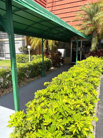 Front view of a building with a green metal awning and surrounding plants.
