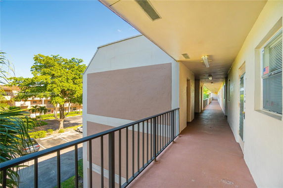 Exterior corridor of an apartment building with view of surrounding trees and parking area.