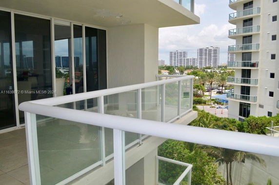 View from a balcony of a high-rise building with glass railings overlooking surrounding urban area with other tall buildings.