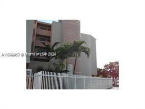 Front view of a multi-story building with a fence and palm trees.