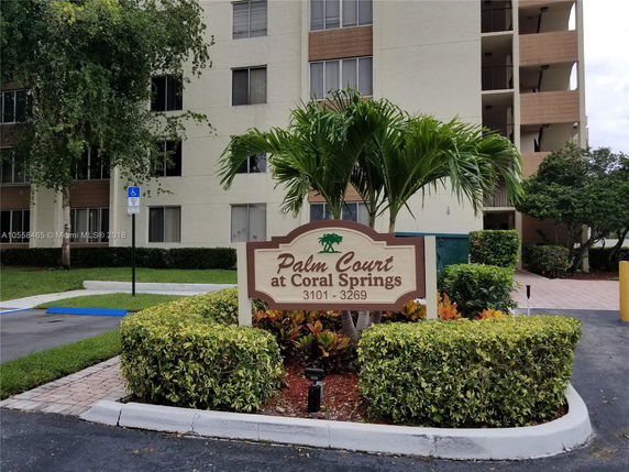 Front view of a multi-story apartment building with a sign reading 'Palm Court at Coral Springs'.