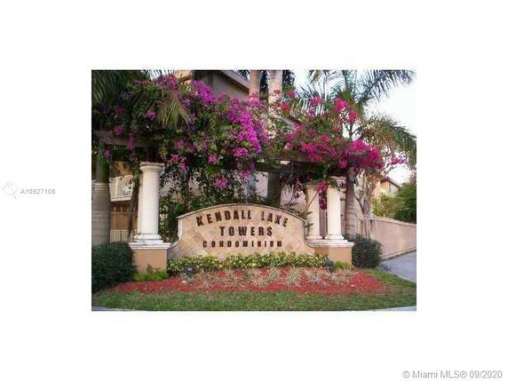 Front view of Kendall Lake Towers Condominium entrance with decorative pillars and flowering plants.