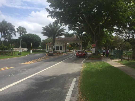 Guardhouse at a gated entrance with road and palm trees.