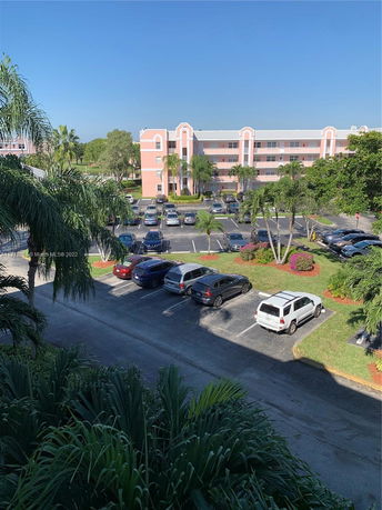 View from above of a parking lot with cars and a multi-story pink residential building in the background.