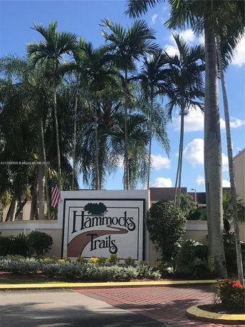 Front view of a building entrance sign with palm trees around.