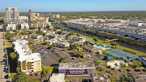 Panoramic view of a cityscape with residential buildings, a canal, parking lots, and tennis courts.