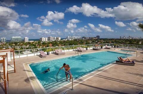 Rooftop swimming pool with lounge chairs around, overlooking cityscape and greenery.