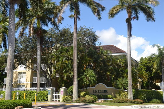 Front view of a residential building with a sign labeled 'Le Club' and surrounded by palm trees.
