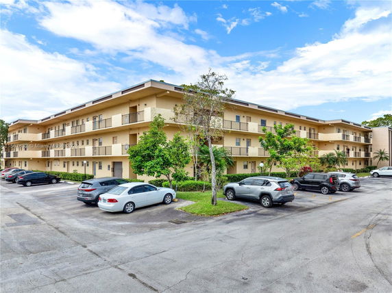 Front view of a three-story apartment building with adjacent parking area.