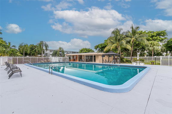 Outdoor swimming pool area with surrounding chairs and greenery.
