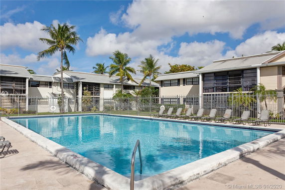 Outdoor swimming pool with surrounding residential buildings and palm trees.