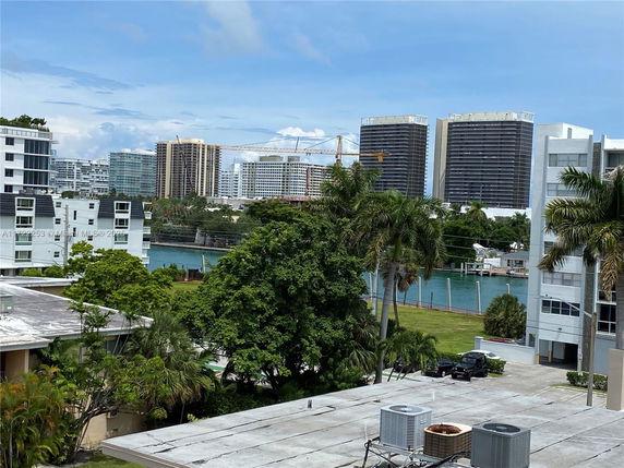 View of buildings across a waterway with a crane in the background and palm trees in the foreground.