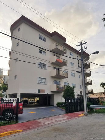 Front view of a multi-story apartment building with balconies and parking area below.