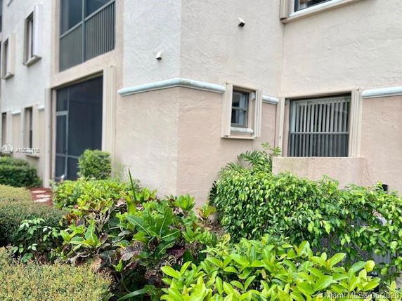Corner view of a multi-story building with small windows and adjacent greenery.