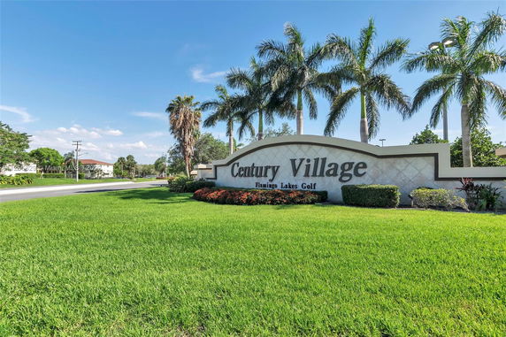 Entrance sign for Century Village surrounded by lush green grass and palm trees.