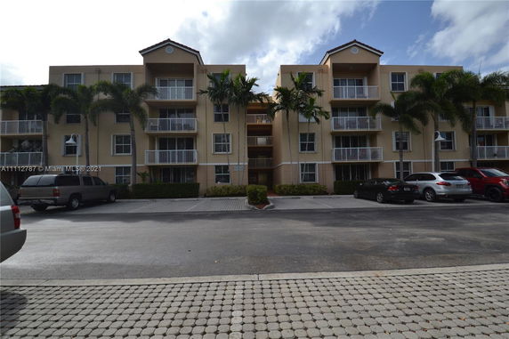 Front view of a multi-story residential building with balconies and palm trees.