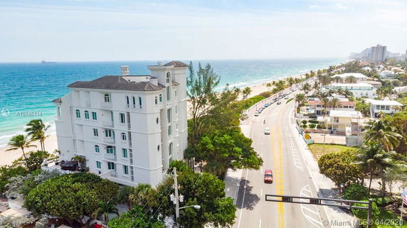 View of a multi-story beachfront building beside a coastal road with ocean and beach scenery.