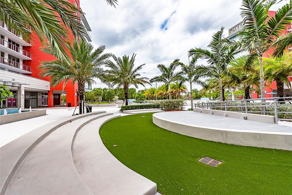 View of a building with red accents and landscaped area with palm trees.