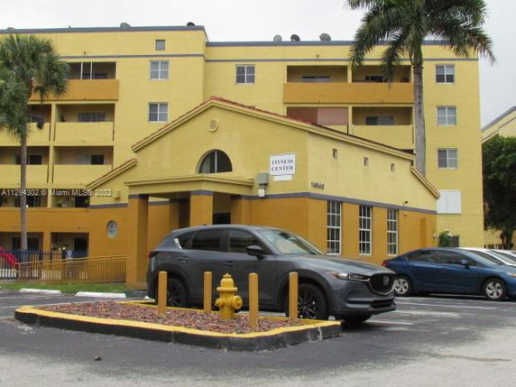 Elevated view of a multi-story yellow building with a fitness center and parking in front.