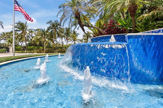 Outdoor view of a blue tiled fountain with water jets and palm trees.
