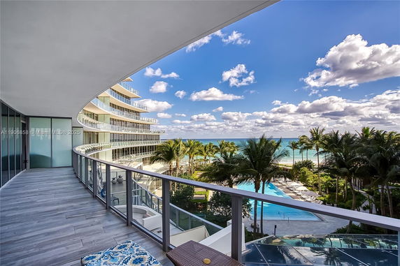 Balcony view from a curved building overlooking the ocean and pool area.