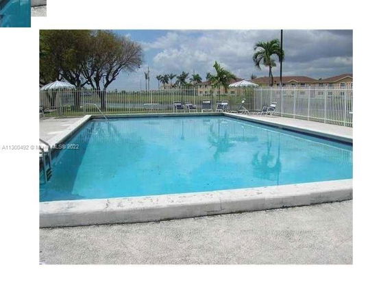 Outdoor swimming pool with surrounding fence and lounge chairs.