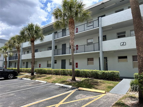 Front view of a three-story apartment building with balconies and palm trees.