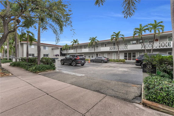 Parking area in front of a two-story building with palm trees.