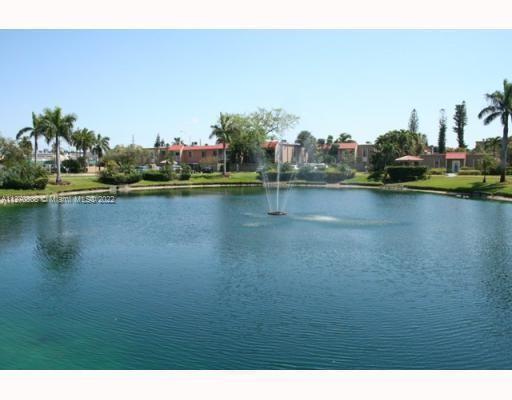 View of a pond with fountains and residential buildings in the background.