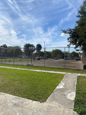 View of a basketball court with a fence and surrounding greenery.