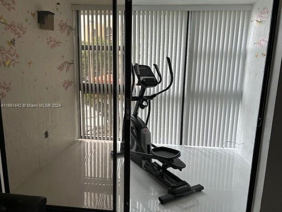 Indoor room with an elliptical exercise machine and vertical blinds on the windows.