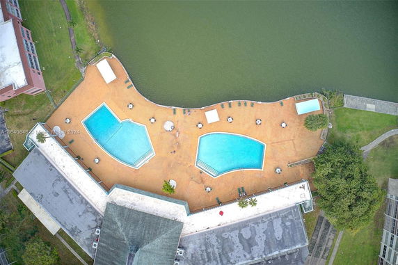 Aerial view of two swimming pools adjacent to a building, situated near a body of water.