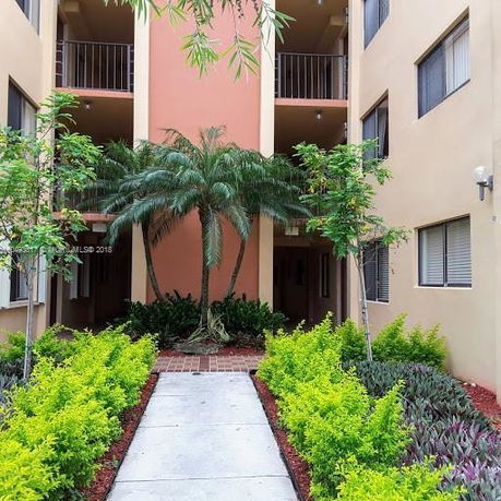 Front view of a multi-story apartment building with balconies and tropical plants.